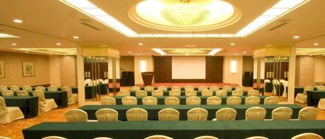 A conference room with rows of tables and chairs, a large screen, and a podium.