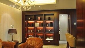 A lobby with a chandelier, a wooden display case with books and bottles, and two upholstered chairs. - Ramada Plaza by Wyndham Shenyang City Center (Shenyang)