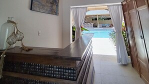 Een modern interieur met een houten plafond, een groot schilderij, uitzicht op een zwembad en een trap naar een balkon.