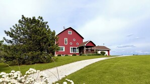 A red house with a porch, surrounded by a grassy field and a gravel path. - Serenity Heights - Peaceful Country Acres with beautiful view in every direction (Osceola)