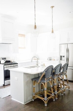 A modern kitchen with white cabinetry, a central island with bar stools, stainless steel appliances, and pendant lighting.
