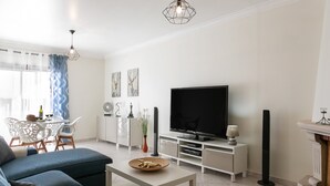 A modern living room with a sofa, a coffee table, a TV, and a dining area with chairs and a table. - O Sítio do Areal - Bright House in Nazaré (Nazaré)