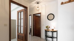 A hallway with wooden doors, a round mirror, a table with a lamp, and a hanging light fixture. - O Sítio do Areal - Bright House in Nazaré (Nazaré)