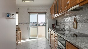 A modern kitchen with wooden cabinets, a granite countertop, and a large window overlooking a cityscape. - O Sítio do Areal - Bright House in Nazaré (Nazaré)