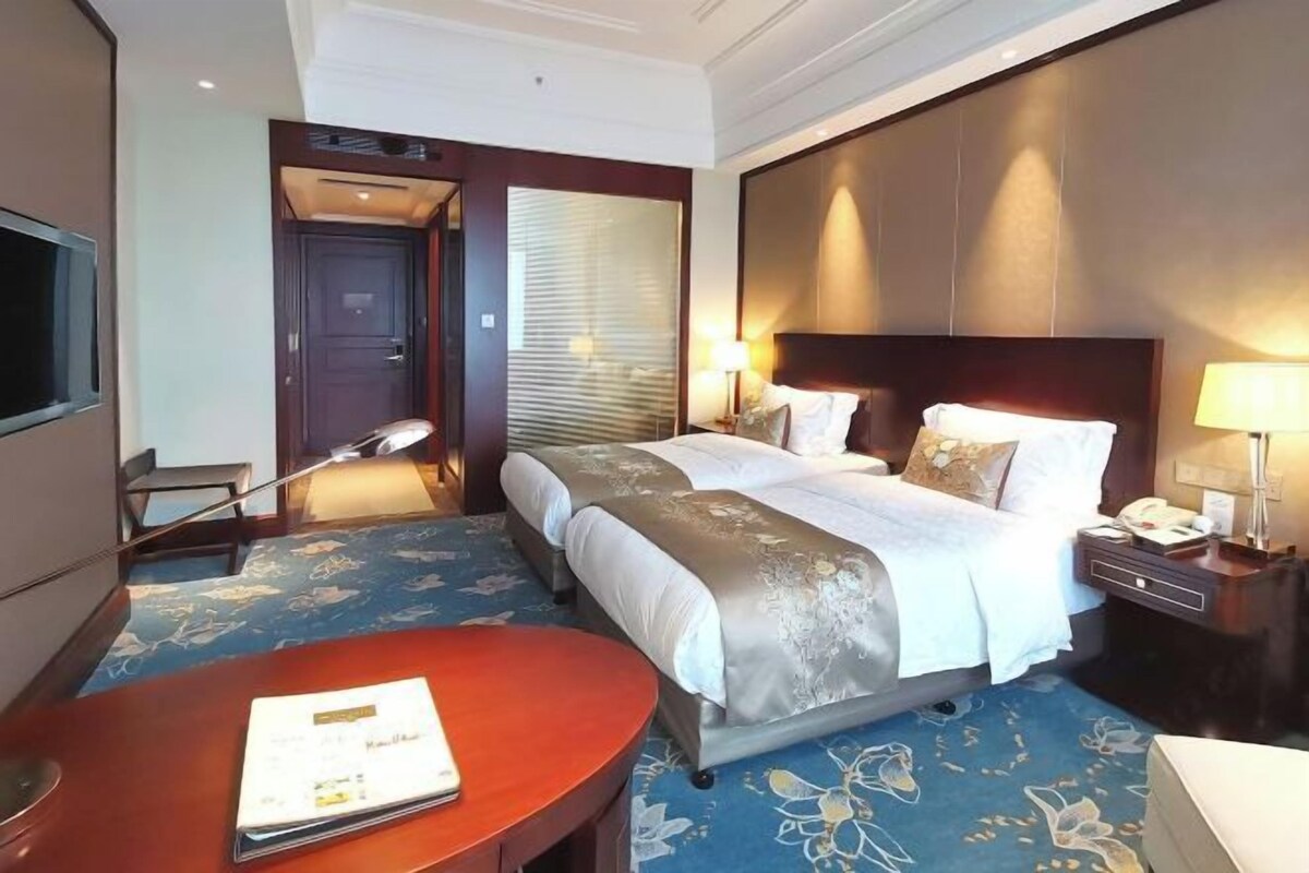 Habitación de hotel con cama doble, escritorio, silla, televisión y ventana con persianas.