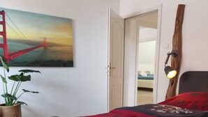 A bedroom with a bed, a potted plant, a painting of the Golden Gate Bridge, and a wooden headboard. - In the forest in a minute. Cozy vacation apartment on the outskirts of the village. (Velen)