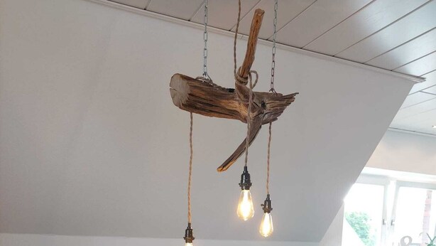 A living room with a brown leather sofa, a wooden coffee table, and a hanging light fixture made of branches. - In the forest in a minute. Cozy vacation apartment on the outskirts of the village. (Velen)