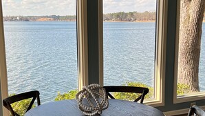 Una mesa redonda con cuatro sillas, un objeto decorativo sobre la mesa, y vistas a un lago a través de tres ventanas.