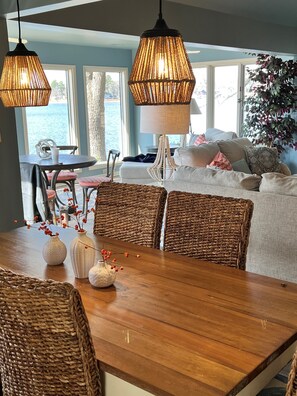 A dining area with a wooden table, wicker chairs, and a view of the water through large windows.