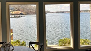 Una habitación con tres ventanas que dan a un lago, una silla y una cama.
