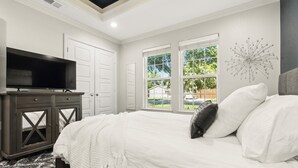 Ein Schlafzimmer mit einem großen Bett, einem Fernseher auf einem Schrank und Blick ins Freie durch große Fenster.