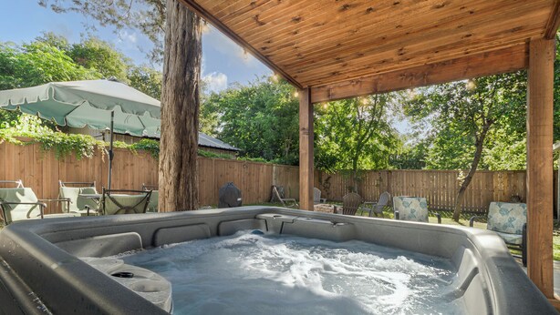 Ein Whirlpool unter einer hölzernen Pergola mit Holzzaun und Stühlen im Hintergrund.