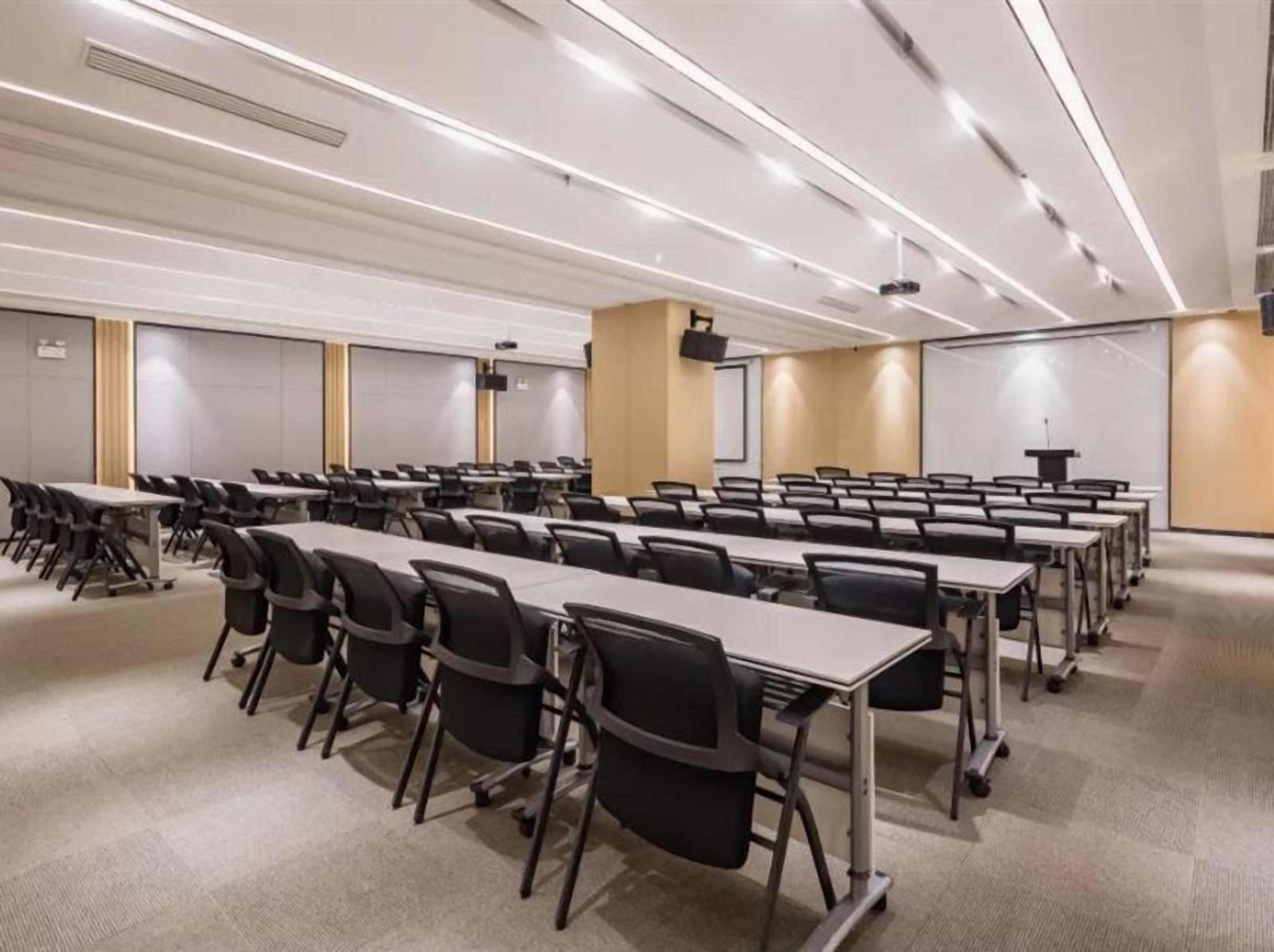 A conference room with rows of tables and chairs, equipped with projectors and screens.