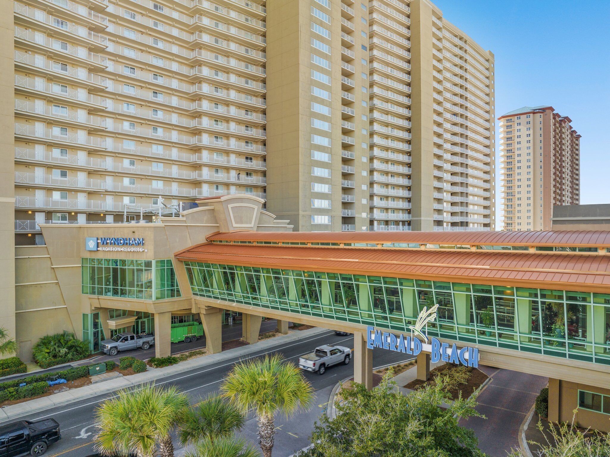 A modern hotel with a prominent glass facade, a covered walkway, and a parking area.