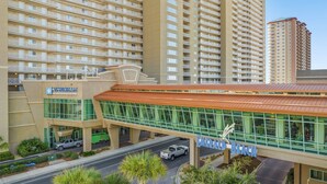 A modern hotel with a prominent glass facade, a covered walkway, and a parking area.