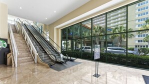 A modern hotel lobby with a central escalator, large glass windows, and a Starbucks sign.