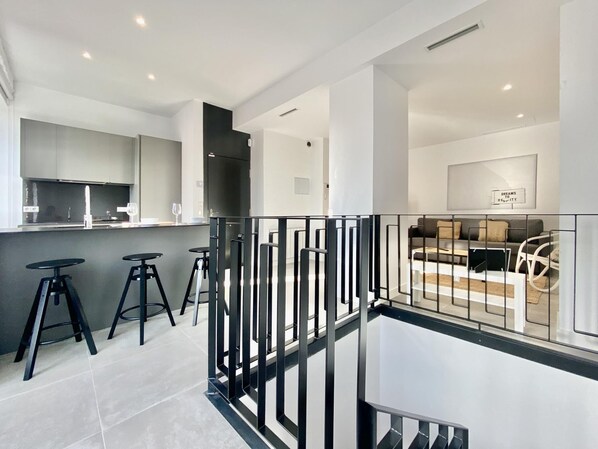 A modern kitchen with a central island, bar stools, and a dining area with a sofa and coffee table.