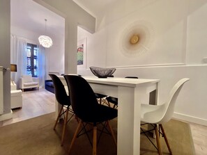 Un espace repas moderne avec une table blanche, des chaises noires et un élément décoratif mural.