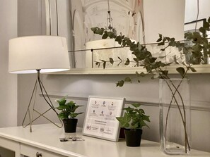 Un bureau blanc avec une lampe, deux plantes en pot et un certificat encadré.