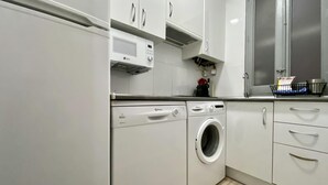 A modern kitchen with white cabinetry, a built-in microwave, and a washing machine. - Malasaña Gallery – 3-Bedroom Apartment in the City Center (Madrid)