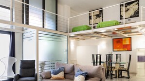 Ein modernes Wohnzimmer mit Sofa, Glastisch und einer Essecke mit Stühlen und Tisch.