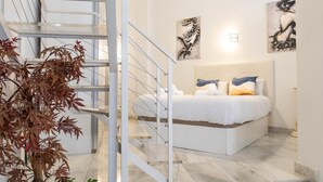 Ein modernes Schlafzimmer mit einem großen Bett, einer Glastreppe und Kunstwerken an den Wänden.