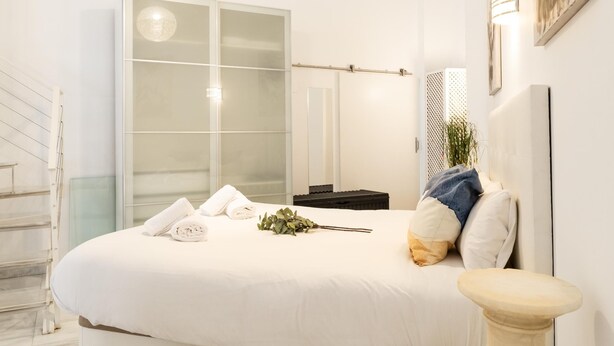 Ein modernes Schlafzimmer mit einem großen Bett, einem Schrank mit Glastüren, einem Nachttisch und einer kleinen Topfpflanze.