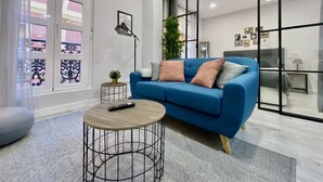 A modern living room with a blue sofa, a round coffee table, and a large window with decorative glass panels. - Madrid Styles - One-bedroom apartment (Madrid)
