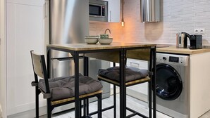 A compact kitchen with a stainless steel refrigerator, a microwave, a washing machine, and a coffee maker on the counter. - Madrid Styles - One-bedroom apartment (Madrid)