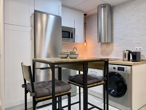 A compact kitchen with a stainless steel refrigerator, a microwave, a washing machine, and a coffee maker on the counter.
