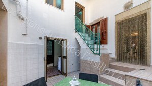 Un patio con una mesa verde, sillas, un farol, una escalera y una puerta que da a un espacio interior.