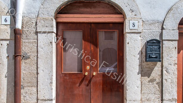 Puerta doble de madera con paneles de vidrio, flanqueada por muros de piedra y placas con números.