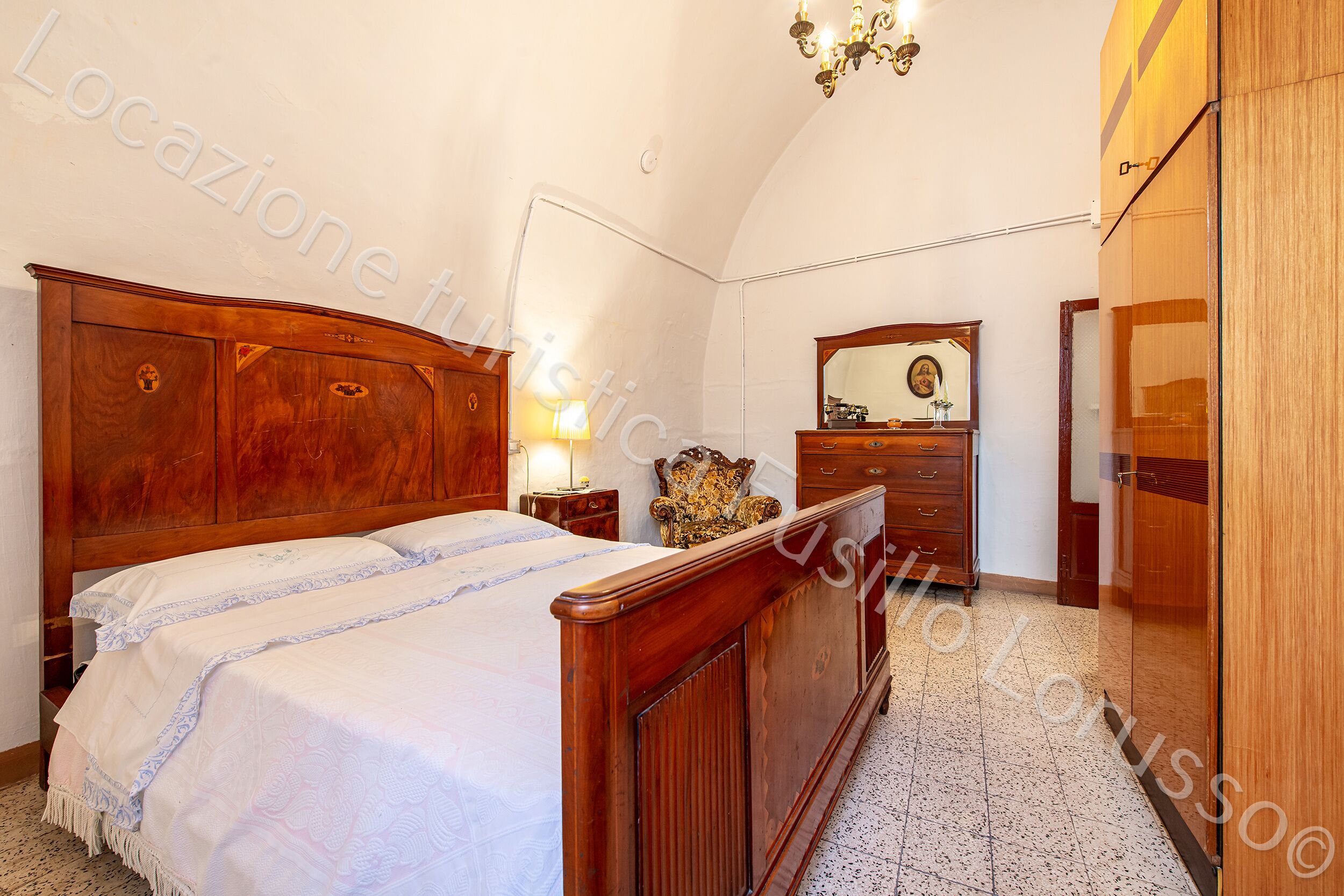 A bedroom with a wooden bed, a dresser, a mirror, and a chandelier.