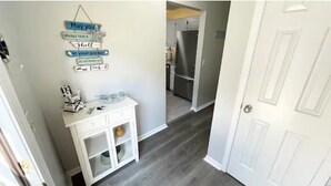 A hallway with a white cabinet, a wall-mounted sign, and a door leading to a kitchen area. - 3 Bed 2.5 Bath, Pet friendly with HotTub, walk to public beach (North Myrtle Beach)