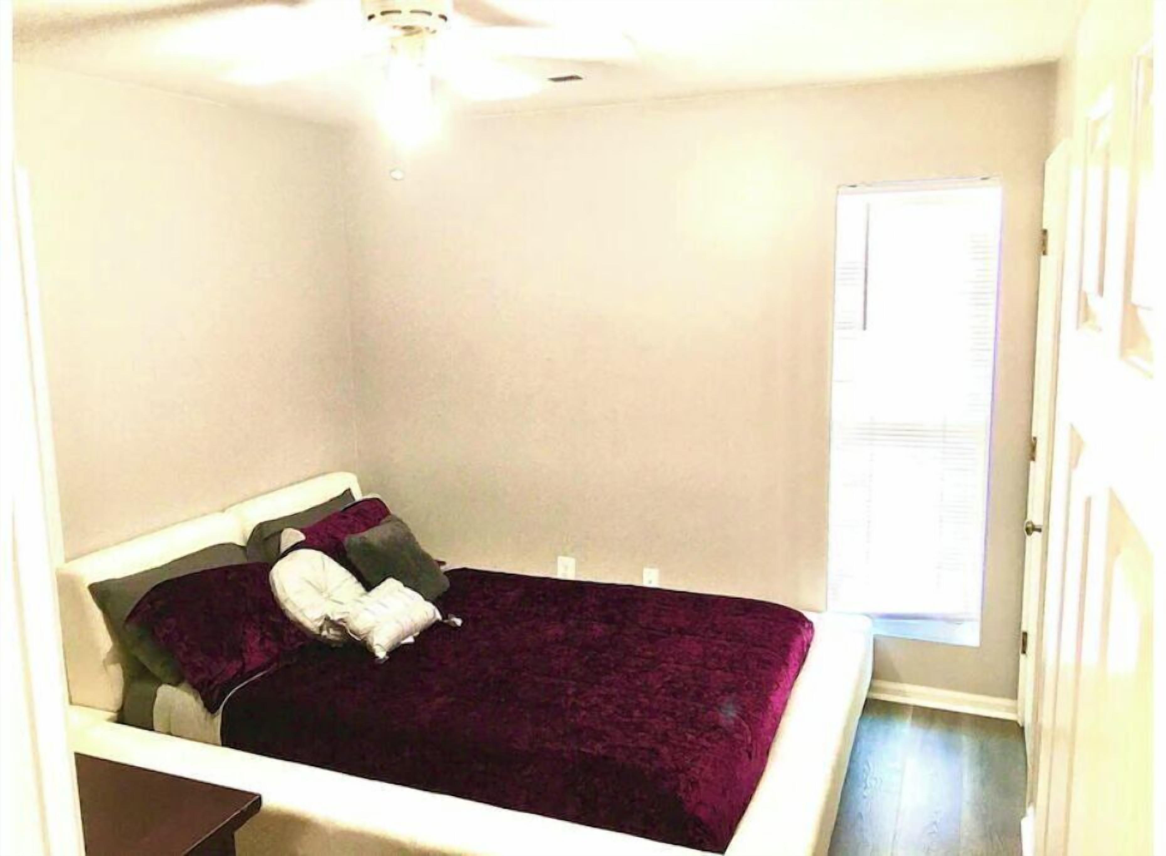 A small, neatly arranged bedroom with a single bed, a window with blinds, and a ceiling fan.