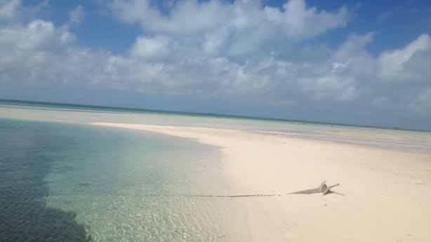 A beach with clear shallow waters and a sandy shore.