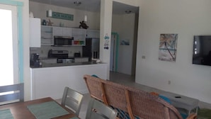 A compact kitchen with white cabinets, a microwave, and a coffee maker. There is a dining area with a table and chairs, and a television mounted on the wall.