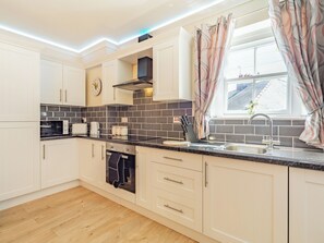 A modern kitchen with white cabinets, a black countertop, and a window with curtains. - Squirrel Cottage - UK37886 (Bishop Auckland)