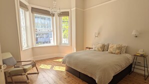 A bedroom with a large bed, a chair, a window with curtains, and a chandelier.