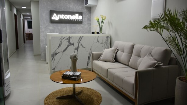 Uma área de recepção com parede de mármore, um sofá, uma mesa de centro e um vaso de planta.