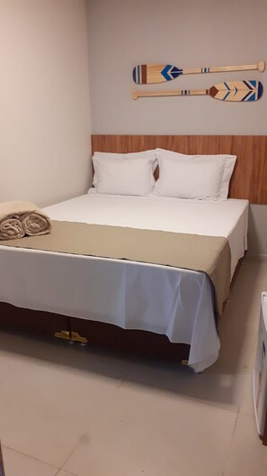 A neatly made bed with white linens and a beige throw blanket, a wooden headboard, and two decorative paddles on the wall. - Pousada Antonella (Maragogi)