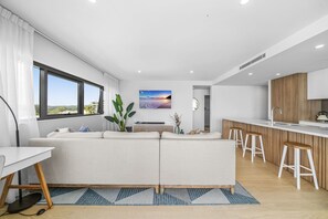A modern living room with a sofa, a dining table, and a kitchen area with stools.