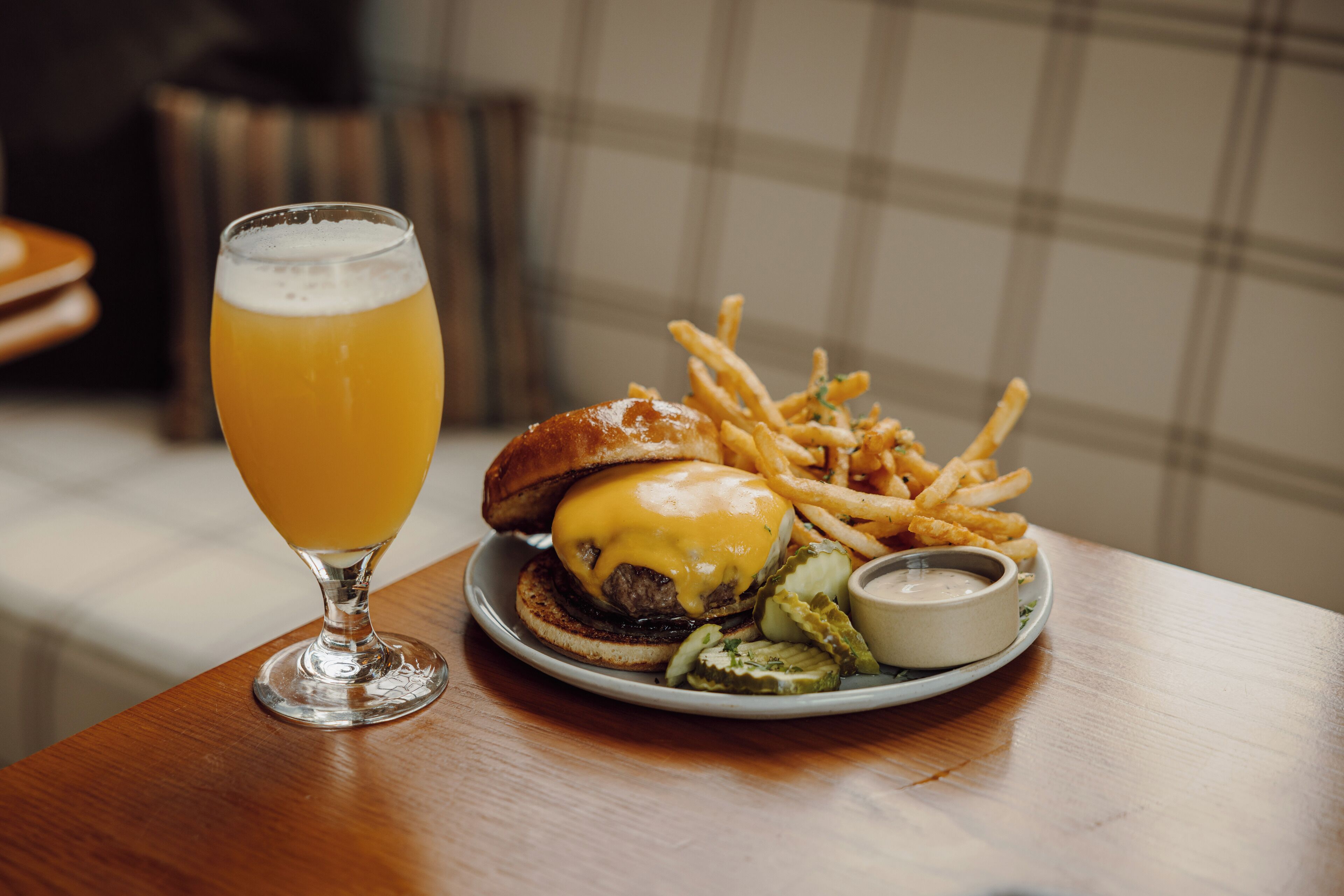 Et måltid bestående af en burger, pommes frites og et glas øl på et træbord.