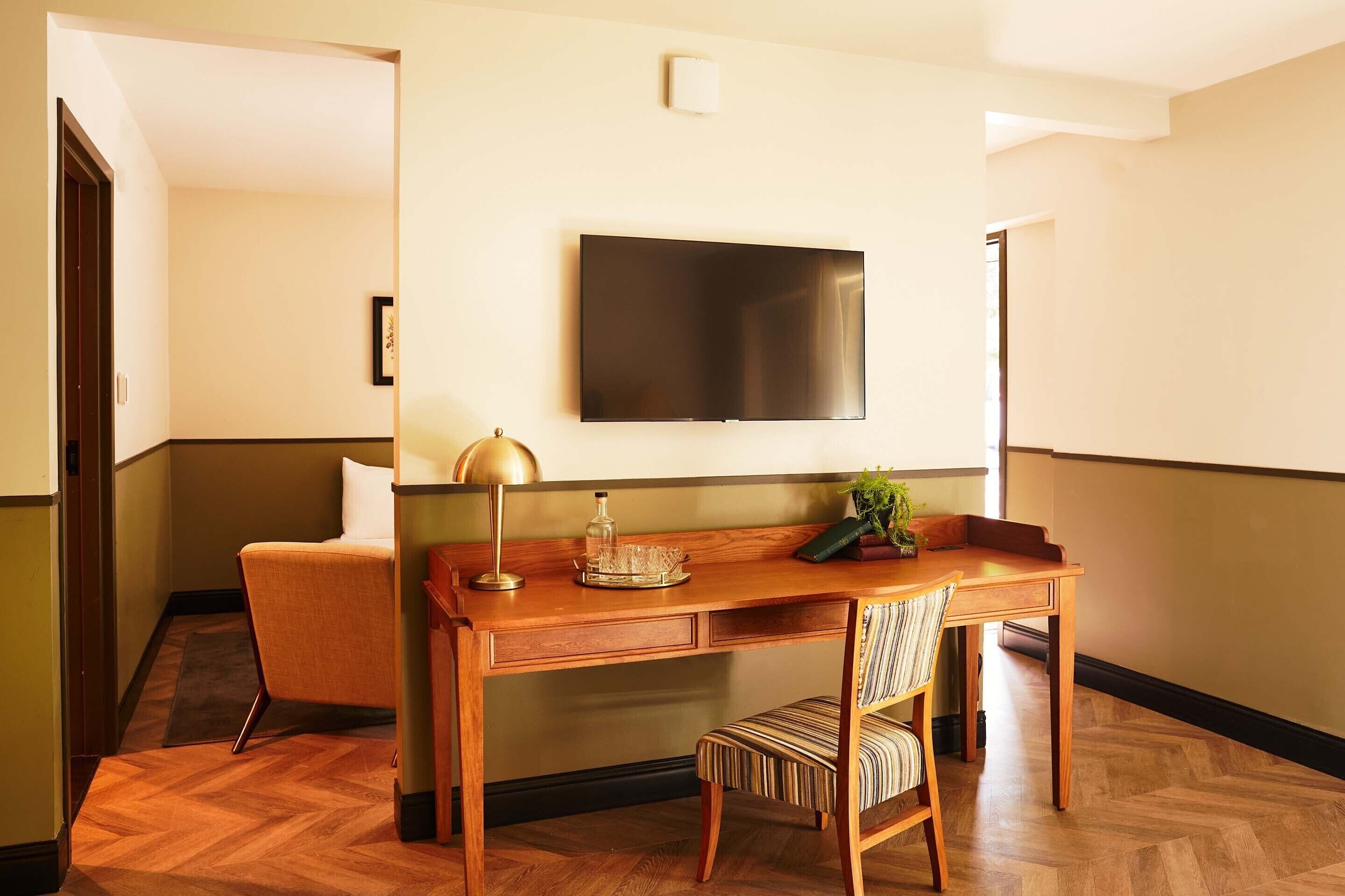 Une chambre d’hôtel avec un bureau en bois, une chaise, un téléviseur fixé au mur et une petite plante en pot.