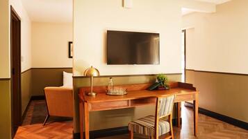 A hotel room with a wooden desk, a chair, a television mounted on the wall, and a small potted plant.
