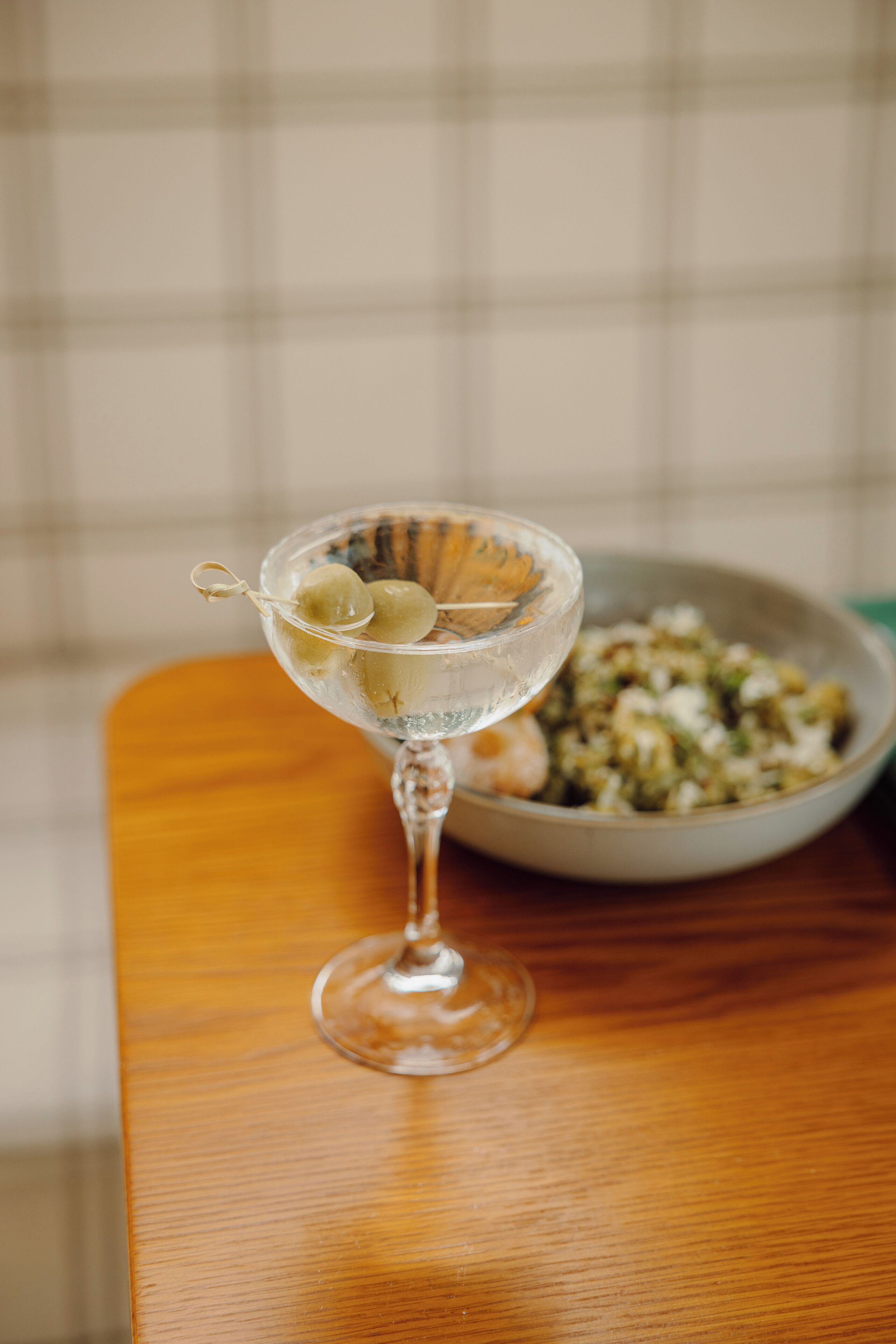 A martini glass with olives on a wooden table.