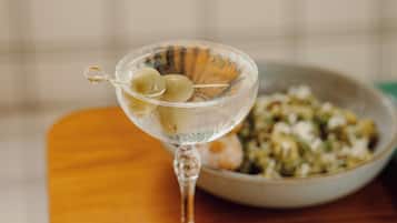 A martini glass with olives on a wooden table.