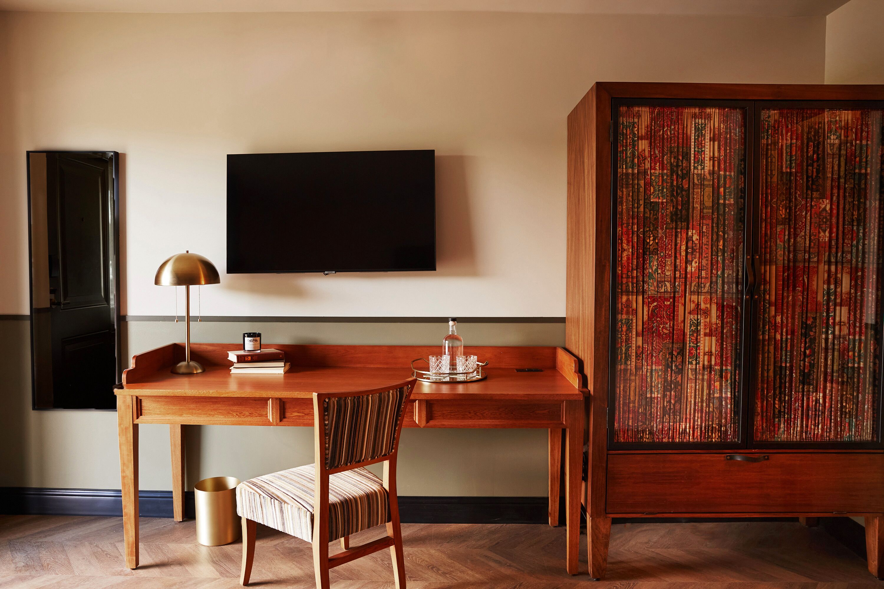Un bureau en bois avec une chaise, un téléviseur fixé au mur et un meuble avec des portes à motifs.