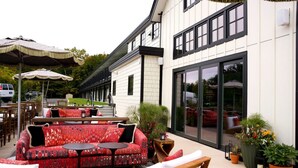 An outdoor seating area with a sofa, chairs, and tables, and a building with large windows and a door labeled "Hotel Entrance". - Berkshires Untold (Lenox)