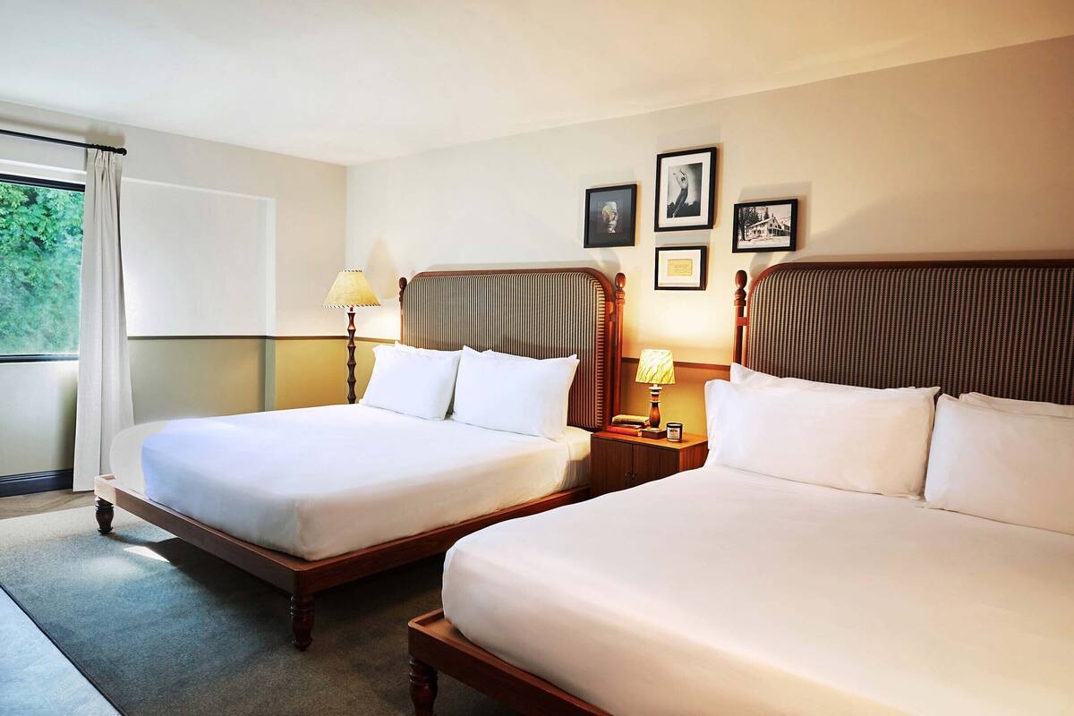 A hotel room with two single beds, a nightstand with a lamp, and framed pictures on the wall.